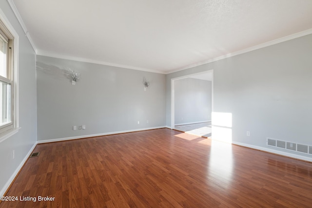 empty room featuring visible vents, crown molding, baseboards, and wood finished floors