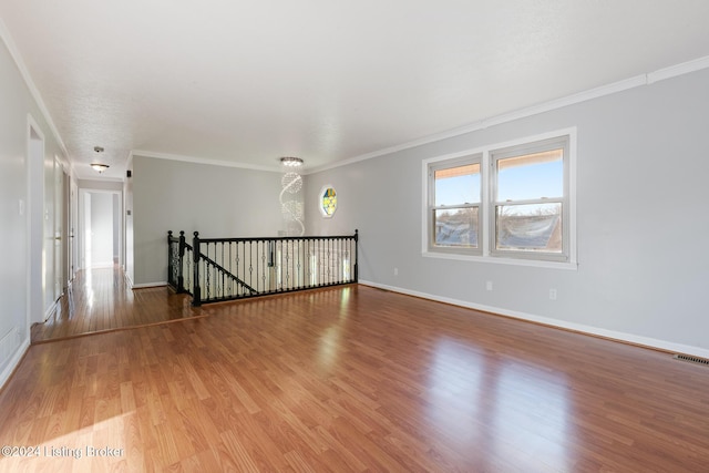 spare room with crown molding, wood finished floors, visible vents, and baseboards