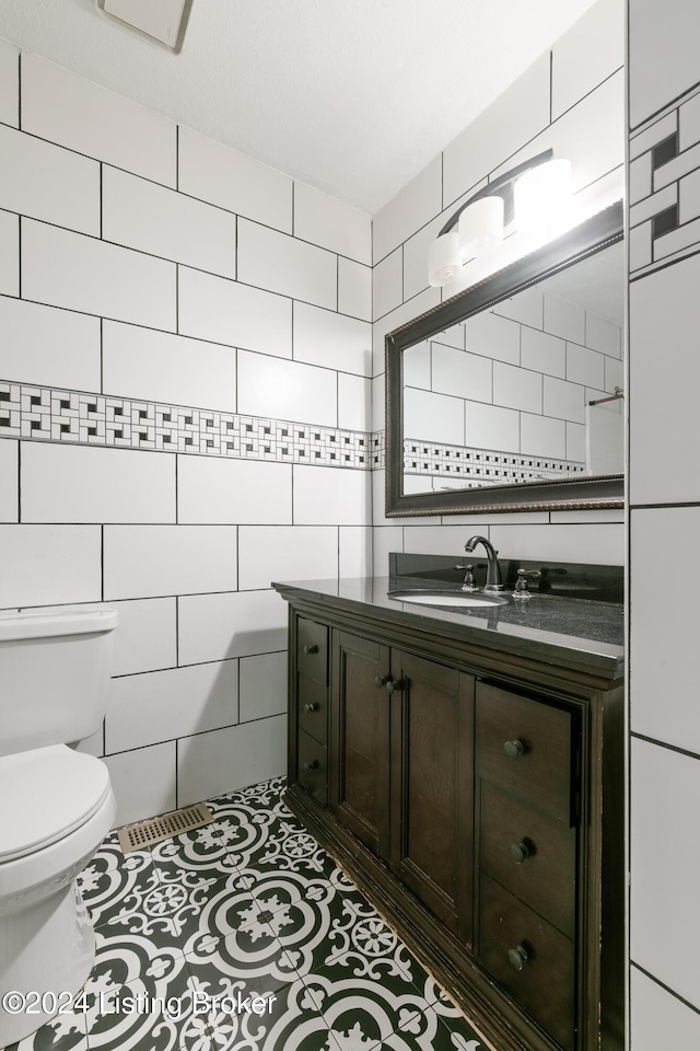 half bathroom with toilet, tile patterned flooring, tile walls, and vanity