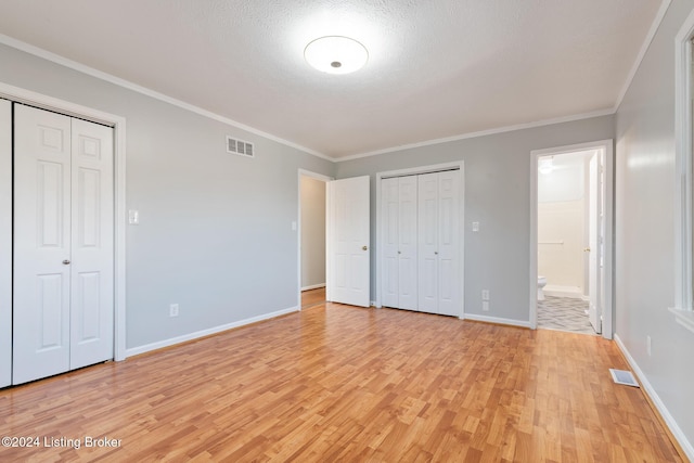 unfurnished bedroom featuring light wood-type flooring, two closets, visible vents, and baseboards