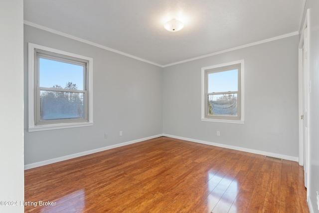 spare room featuring ornamental molding, baseboards, visible vents, and hardwood / wood-style floors