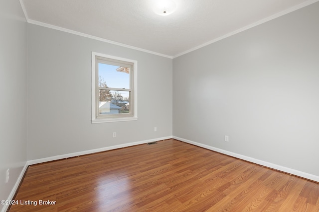 unfurnished room featuring ornamental molding, wood finished floors, visible vents, and baseboards