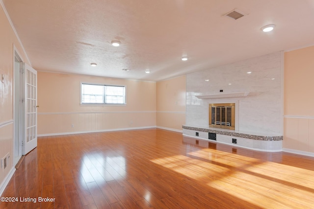 unfurnished living room with a textured ceiling, a wainscoted wall, a fireplace, wood finished floors, and visible vents