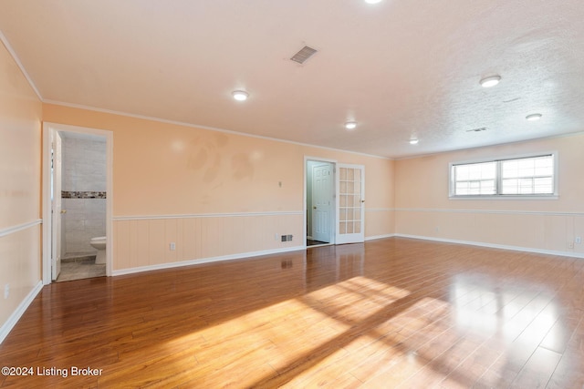 empty room with a wainscoted wall, a textured ceiling, wood finished floors, and visible vents