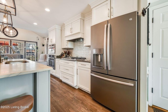 kitchen with custom range hood, dark wood-style flooring, vaulted ceiling, stainless steel appliances, and a sink