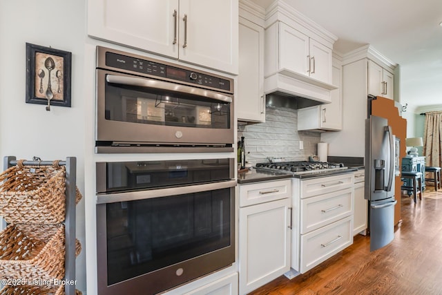 kitchen with premium range hood, appliances with stainless steel finishes, backsplash, dark wood-style floors, and dark countertops