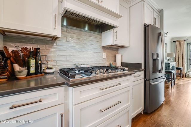 kitchen featuring stainless steel appliances, dark countertops, decorative backsplash, wood finished floors, and premium range hood