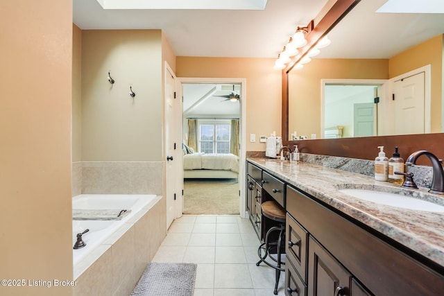 ensuite bathroom with double vanity, a skylight, tile patterned flooring, tiled tub, and a sink