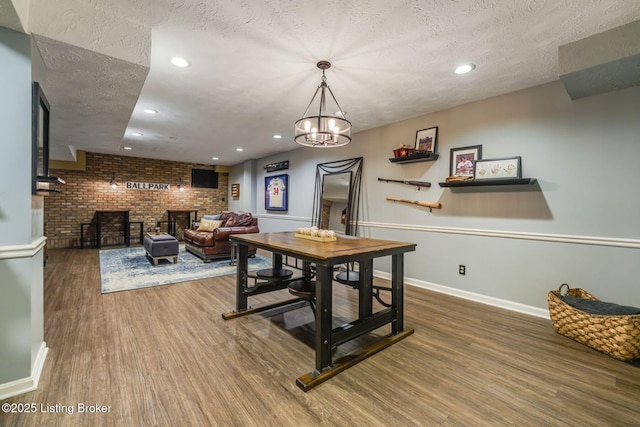 dining room featuring a fireplace, a textured ceiling, brick wall, wood finished floors, and baseboards