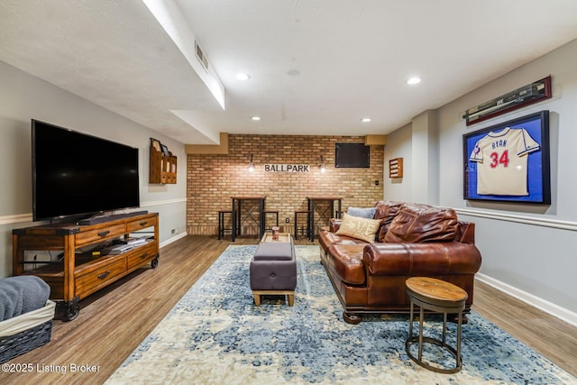 living area featuring brick wall, wood finished floors, visible vents, and baseboards