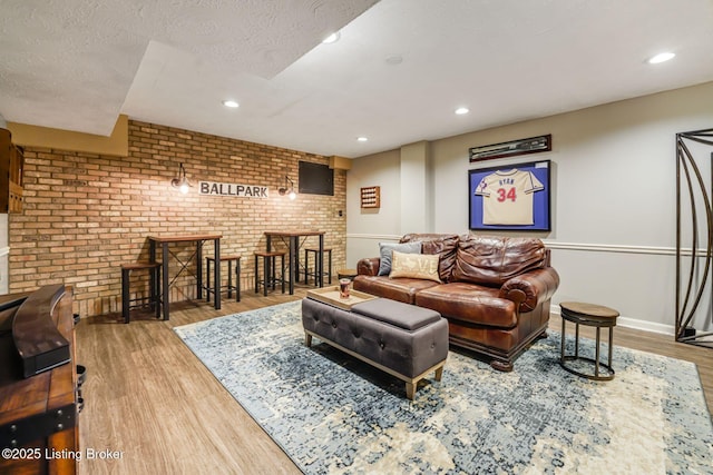 living room featuring a textured ceiling, recessed lighting, brick wall, wood finished floors, and baseboards