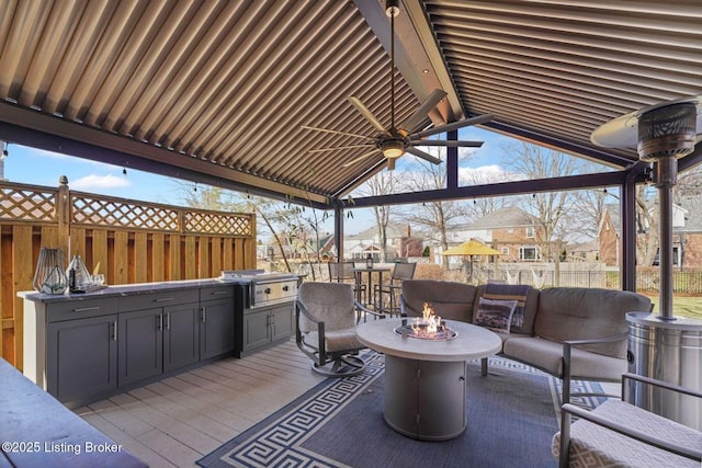 wooden terrace featuring an outdoor living space with a fire pit, grilling area, a ceiling fan, fence, and exterior kitchen