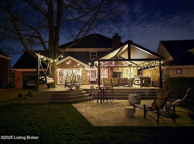 back of house at night featuring a wooden deck, a chimney, and a gazebo