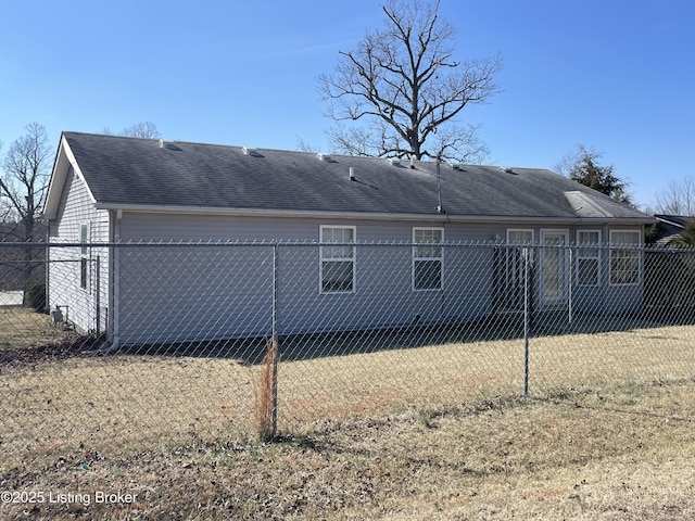 back of house featuring a shingled roof, fence, and a lawn