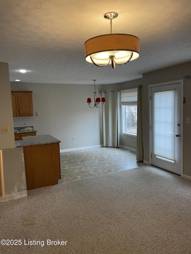 interior space featuring light carpet, baseboards, brown cabinetry, a kitchen island, and a textured ceiling