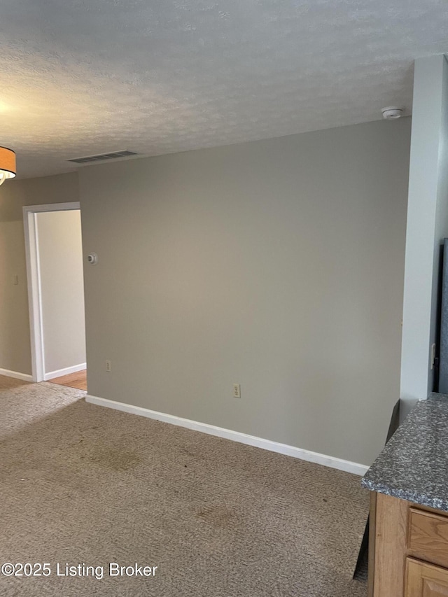 unfurnished room featuring visible vents, light colored carpet, a textured ceiling, and baseboards