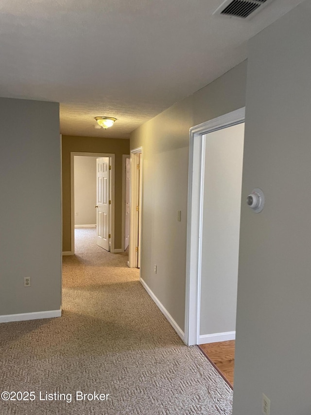 corridor featuring baseboards, visible vents, and carpet flooring