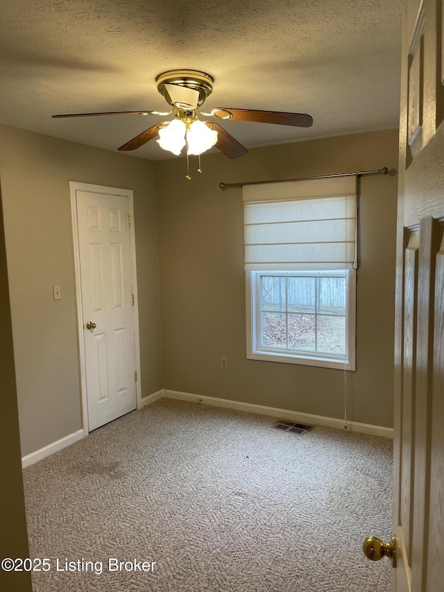 empty room with a textured ceiling, carpet flooring, a ceiling fan, visible vents, and baseboards