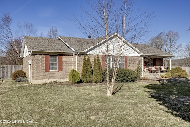 view of front of home with brick siding, roof with shingles, a front yard, and fence