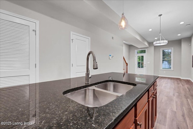 kitchen featuring dark stone counters, wood finished floors, pendant lighting, a sink, and recessed lighting