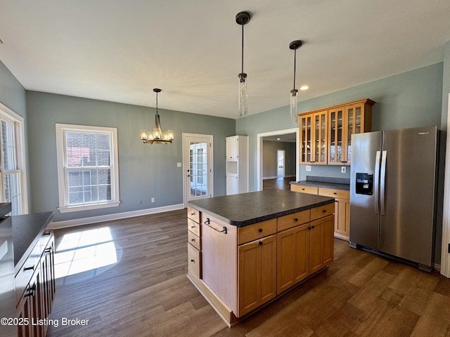 kitchen featuring dark wood finished floors, stainless steel fridge with ice dispenser, glass insert cabinets, pendant lighting, and dark countertops