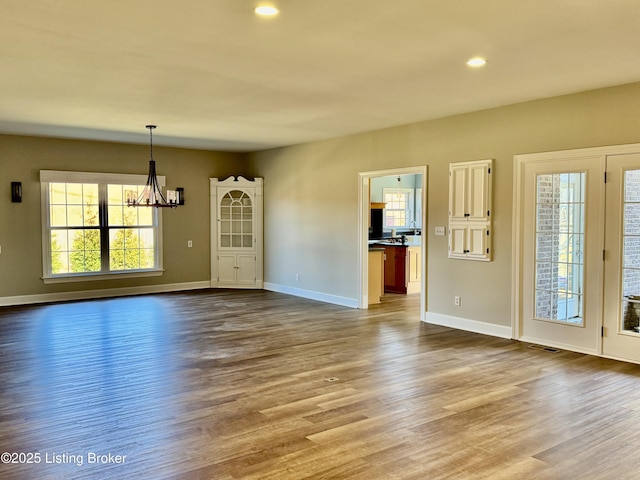 unfurnished living room featuring an inviting chandelier, visible vents, dark wood-type flooring, and baseboards