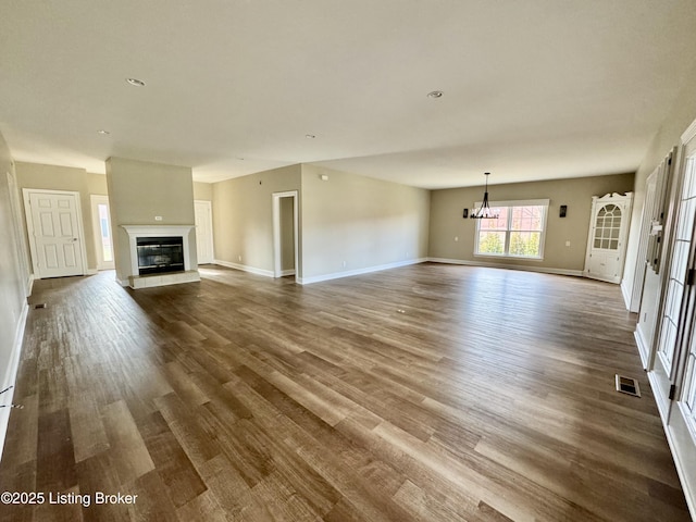 unfurnished living room featuring dark wood-style floors, a glass covered fireplace, baseboards, and visible vents