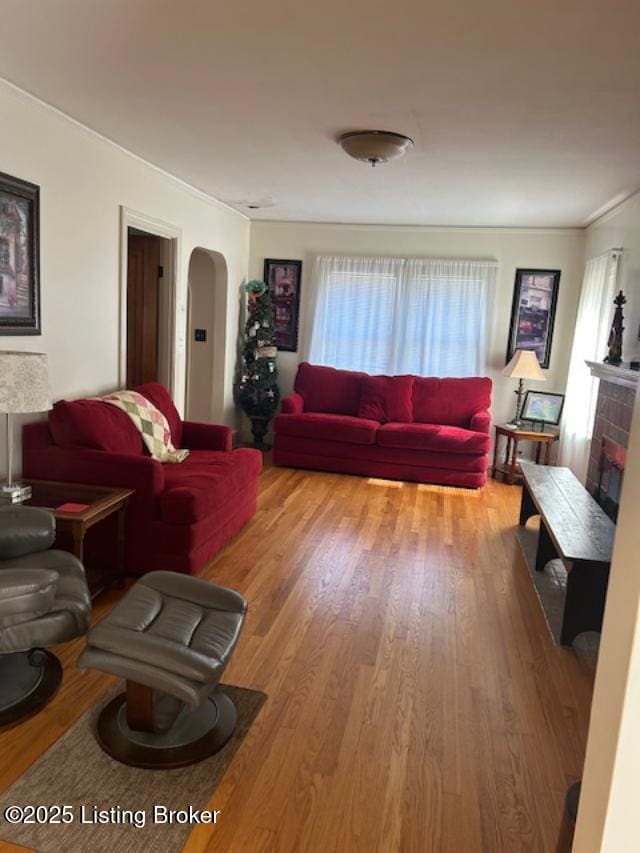 living area with arched walkways, a fireplace with raised hearth, and wood finished floors