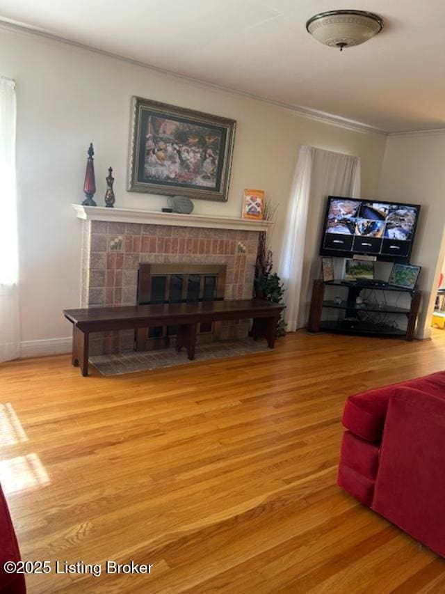 living room with crown molding, a fireplace, baseboards, and wood finished floors