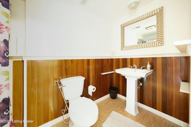 bathroom featuring a wainscoted wall, wood walls, and toilet