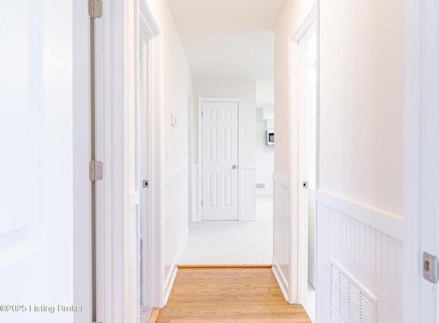 hallway with light wood finished floors, visible vents, and a wainscoted wall