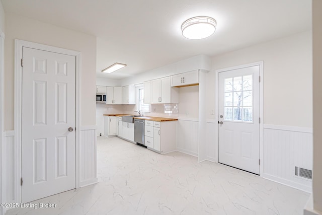 kitchen with stainless steel appliances, visible vents, white cabinetry, marble finish floor, and wainscoting