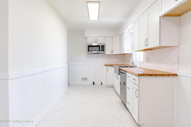 kitchen featuring a wainscoted wall, visible vents, marble finish floor, appliances with stainless steel finishes, and backsplash