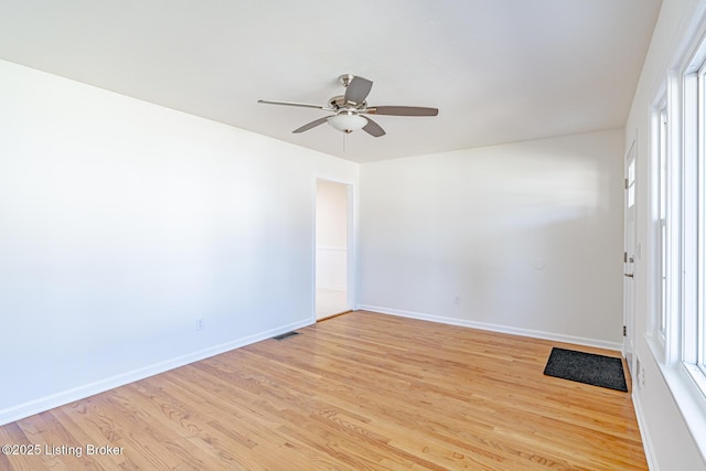 empty room with ceiling fan, light wood finished floors, a healthy amount of sunlight, and baseboards