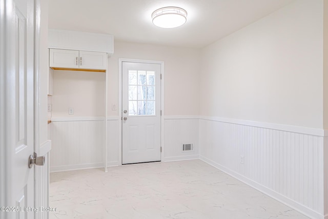 interior space featuring marble finish floor, visible vents, and a wainscoted wall