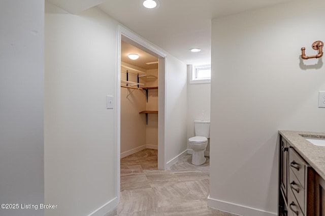 full bath featuring baseboards, toilet, a walk in closet, vanity, and recessed lighting