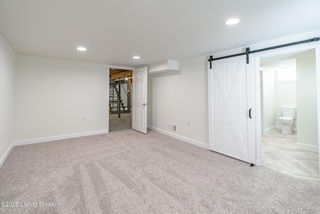 basement with light carpet, a barn door, stairs, and visible vents