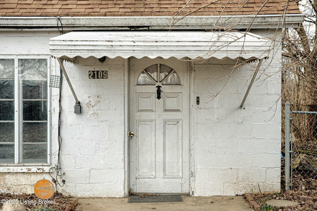 entrance to property featuring a shingled roof and concrete block siding