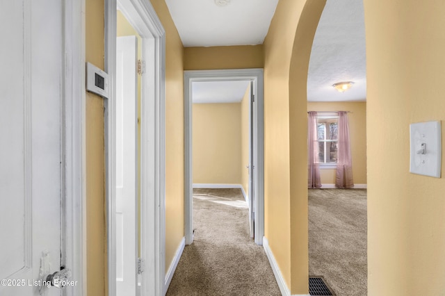 hall featuring carpet, arched walkways, and baseboards