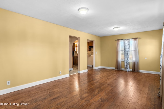 spare room featuring baseboards, arched walkways, and hardwood / wood-style floors