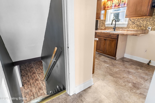 interior space with brown cabinetry, a sink, backsplash, and baseboards