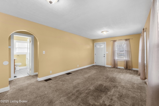 unfurnished room featuring carpet floors, baseboards, visible vents, and arched walkways