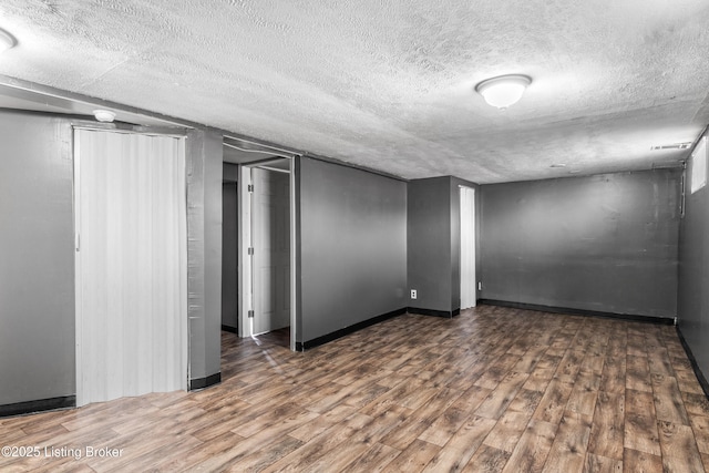 empty room with a textured ceiling, wood finished floors, and baseboards