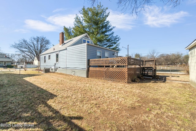 view of side of property with central air condition unit, fence, a yard, a wooden deck, and a chimney