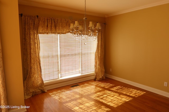 unfurnished room with ornamental molding, a notable chandelier, baseboards, and wood finished floors