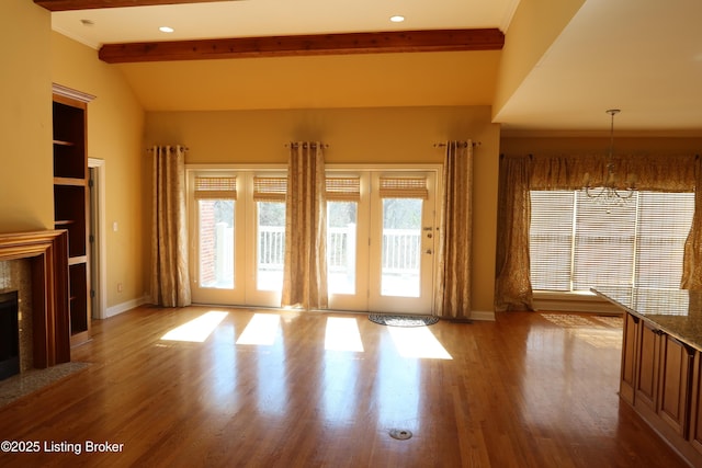 unfurnished living room featuring vaulted ceiling with beams, a premium fireplace, wood finished floors, and baseboards