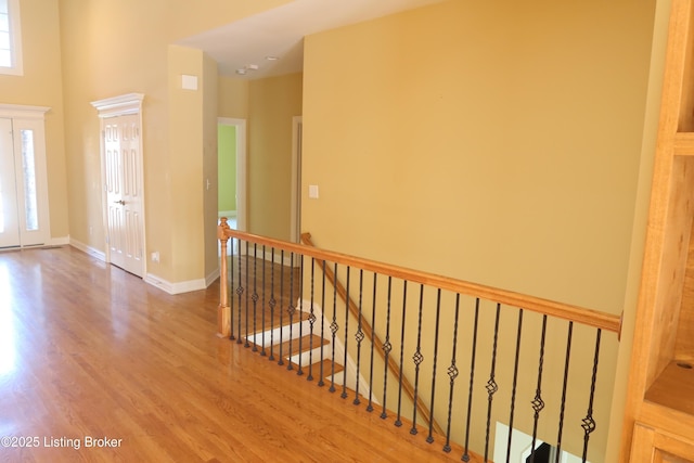 hallway featuring a healthy amount of sunlight, baseboards, wood finished floors, and an upstairs landing