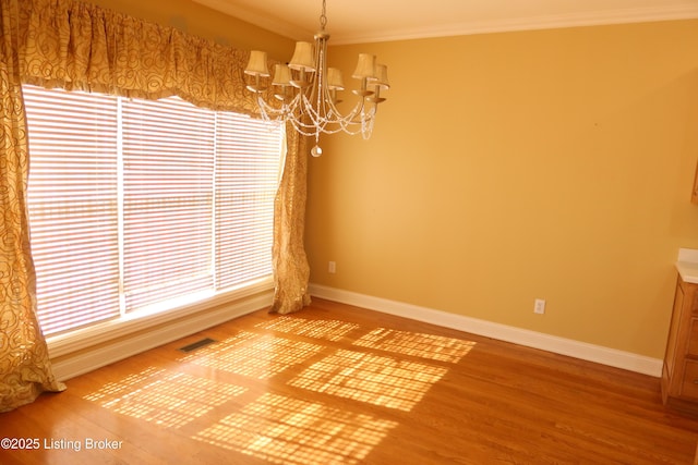 spare room featuring a chandelier, ornamental molding, wood finished floors, and baseboards