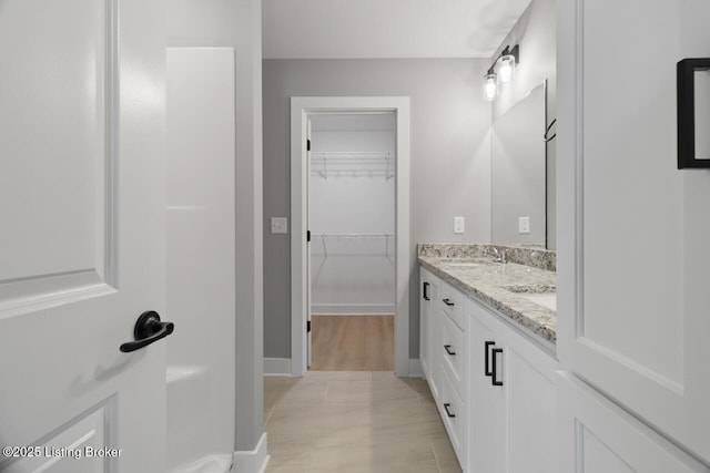 full bath with double vanity, a spacious closet, a sink, and baseboards