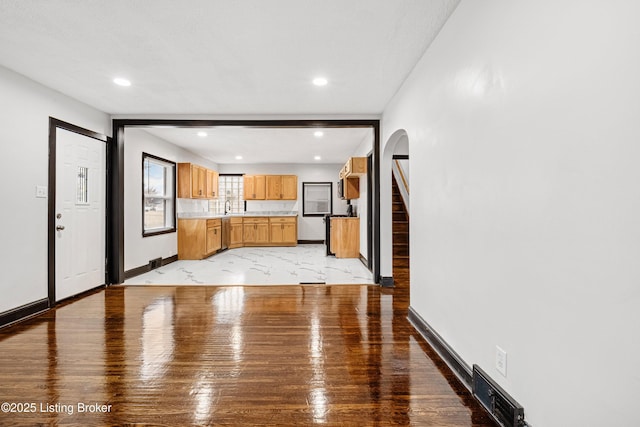 unfurnished living room with arched walkways, recessed lighting, a sink, visible vents, and baseboards